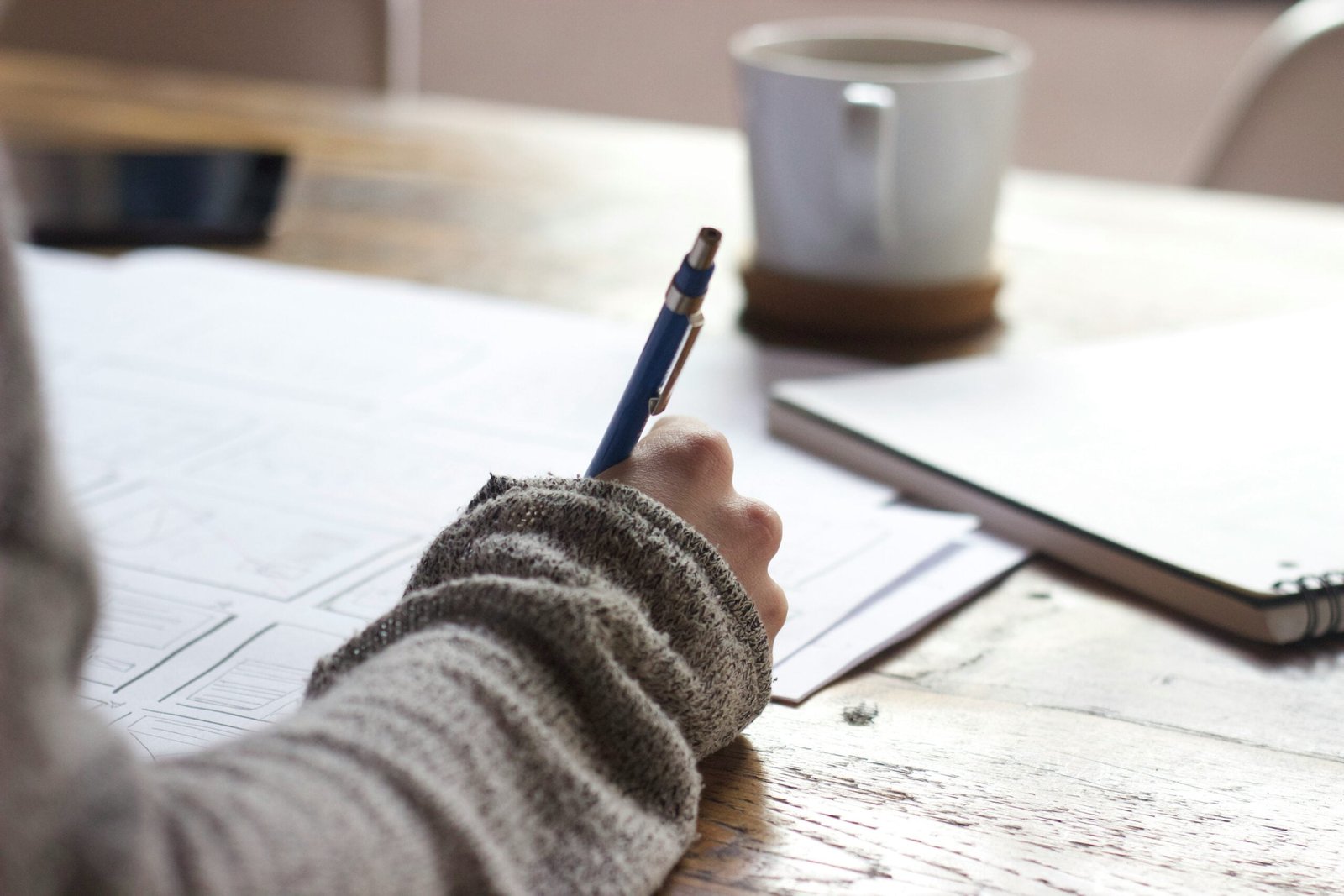 content creators: person writing on brown wooden table near white ceramic mug